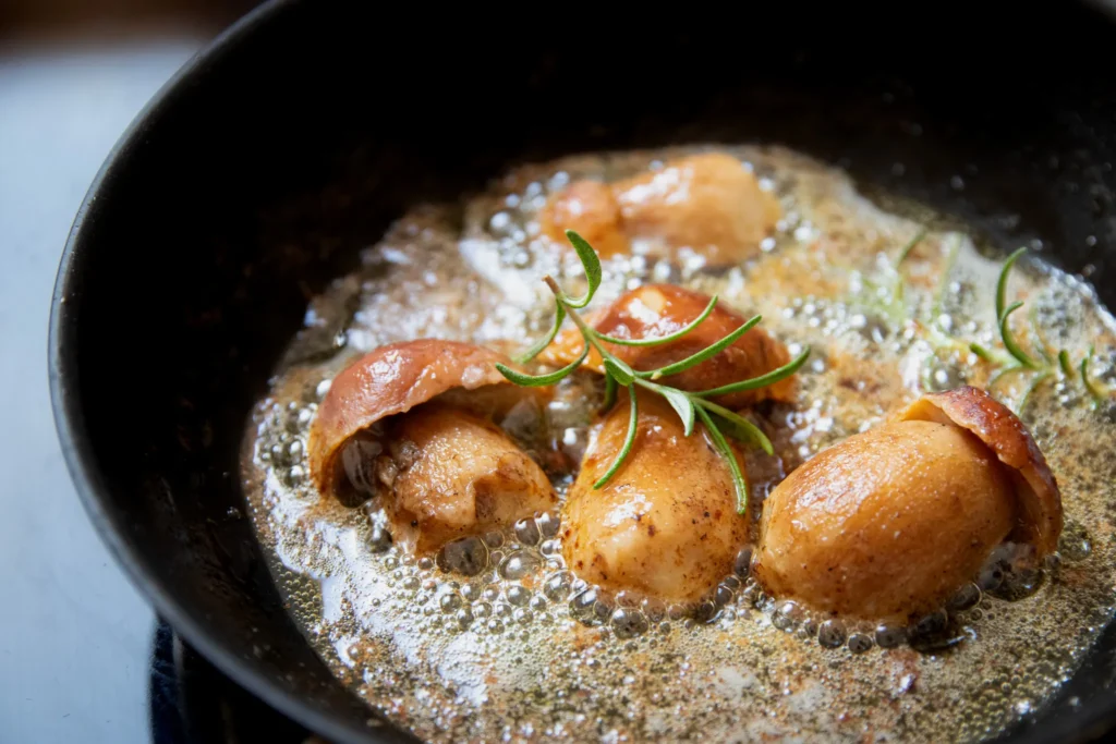 Steinpilze zubereiten: halbierte Steinpilze mit Rosmarin in schäumender Butter in der Pfanne