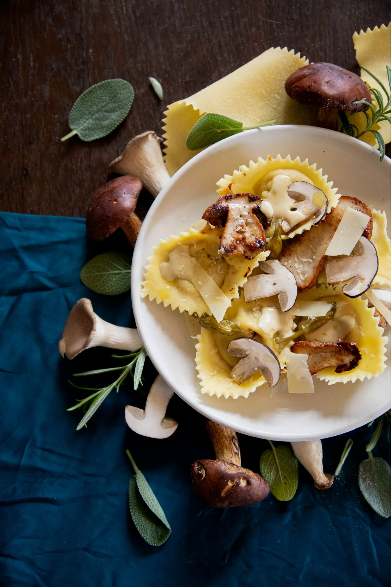 Selbstgemachte Steinpilz-Tortelloni mit Salbei, Rosmarin und gehobeltem Käse auf einem Teller, von oben fotografiert